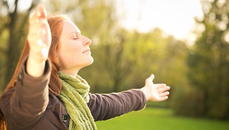 Woman worshiping with open arms or taking in the Autumn sun in a park.